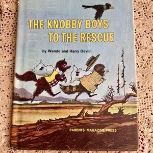 May include: Vintage children's book titled "The Knobby Boys to the Rescue" by Wende and Harry Devlin. The cover features an illustration of three animal characters running across a landscape, with a bird flying above. Published by Parents' Magazine Press.