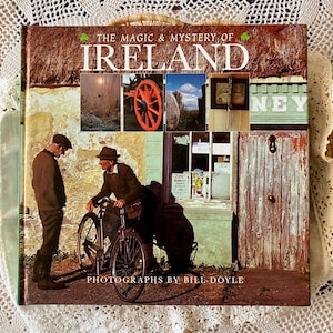 May include: A hardcover book titled "The Magic & Mystery of Ireland" featuring photographs by Bill Doyle. The cover displays a collage of Irish scenes, including a thatched roof, an orange cartwheel, and two men with a bicycle.