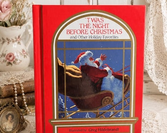 May include: A red hardcover book titled 'Twas the Night Before Christmas and Other Holiday Favorites, illustrated by Greg Hildebrandt. The cover features a gold-framed illustration of Santa Claus in a sleigh against a blue night sky.