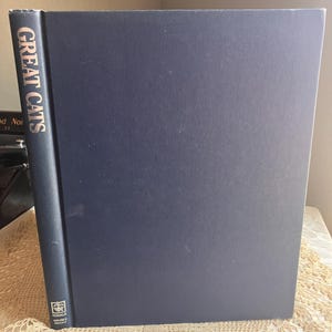 May include: A large, dark blue hardcover book titled GREAT CATS printed in gold lettering on the spine. The book features a small Rodale Nature Animals logo at the bottom of the spine. The cover is solid dark blue with no other visible text or images.