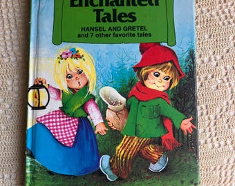 May include: A hardcover book titled Enchanted Tales: Hansel and Gretel and 7 other favorite tales. The cover features an illustration of two children in a forest, one holding a lantern and the other a sack, with a Honey Bear Books logo at the top.