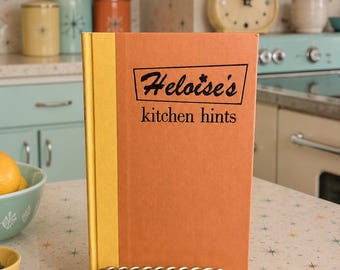 May include: A hardcover book titled Heloise's kitchen hints with a burnt orange cover and a yellow spine. The title is printed in black text inside a trapezoidal border. The book is displayed upright on a gold-toned, twisted metal stand.