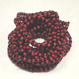May include: A coiled strand of small, round beads arranged in an alternating pattern of glossy black and vibrant red colors. The beads are strung together in a continuous loop, creating a dense, circular formation with a hollow center.