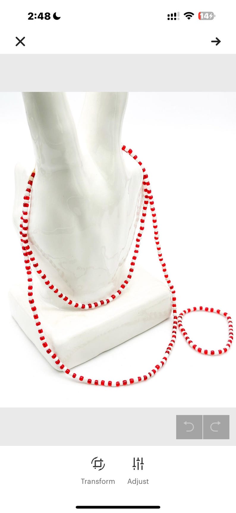 Op de afbeelding: Een lange ketting en een bijpassende armband gemaakt van kleine, afwisselend rode en witte cilindrische kralen. De sieradenset heeft een consistent patroon van individuele rode kralen gescheiden door enkele witte kralen over de gehele lengte.