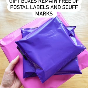 May include: Three purple mailing envelopes are stacked on top of a pink mailing envelope. The text on the top of the image reads "SENT IN POSTAL BAGS SO THE GIFT BOXES REMAIN FREE OF POSTAL LABELS AND SCUFF MARKS."