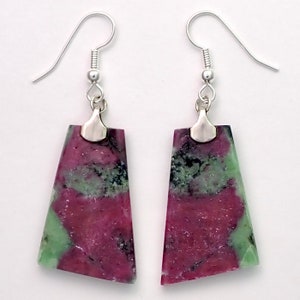 May include: A pair of silver earrings with green and pink gemstone drops. The gemstones are a mix of green and pink with black flecks.
