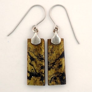 May include: A pair of gold and black rectangular earrings with silver hooks. The earrings have a marbled pattern.