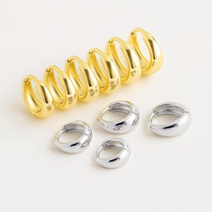 May include: A collection of gold and silver hoop earrings. The gold earrings are in a row, with the silver ones grouped below. The earrings have a smooth, polished finish and a classic, rounded design. The earrings are suitable for everyday wear.