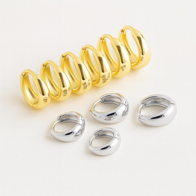 May include: A collection of gold and silver hoop earrings. The gold earrings are in a row, with the silver ones grouped below. The earrings have a smooth, polished finish and a classic, rounded design. The earrings are suitable for everyday wear.