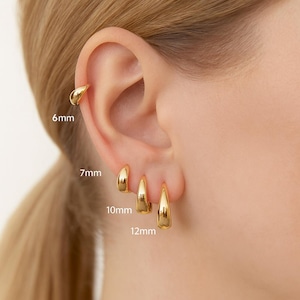 May include: A close-up of an ear displaying gold-coloured hoop earrings. The image shows four sizes: 6mm, 7mm, 10mm, and 12mm. The earrings have a smooth, polished finish, reflecting light.