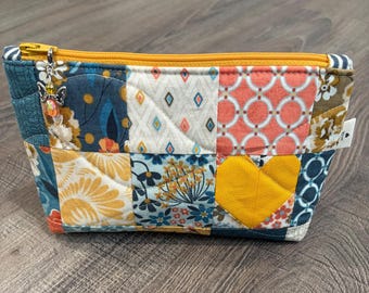 May include: A quilted patchwork pouch with a yellow zipper and butterfly charm. The pouch features a variety of fabric patterns, including floral, geometric, and a yellow heart. The pouch is approximately 8 inches long and 4 inches high.