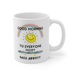 Puede incluir: Taza de café de cerámica blanca con un gráfico de arcoíris, sol y nubes. El texto dice "Good Morning to Everyone Except Greg Abbott".