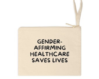 Puede incluir: Una bolsa de lona beige con cremallera y asa negra. La bolsa tiene el texto "GENDER-AFFIRMING HEALTHCARE SAVES LIVES" impreso en negro.