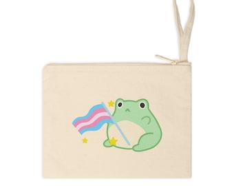 Puede incluir: Una bolsa de lona beige con cremallera con una rana verde sosteniendo una bandera del orgullo transgénero. La rana está rodeada de pequeñas estrellas amarillas.