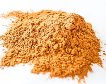 May include: A pile of loose, finely ground, orange-brown powder on a white surface.
