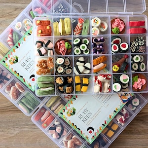 May include: Clear plastic organizer boxes filled with miniature sushi-themed beads. The beads are various colors and shapes, including rolls, nigiri, and sashimi. The boxes have the text "RUBY KEEN" on the label.