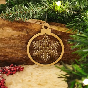 Könnte beinhalten: Ein hölzerner Weihnachtsbaumschmuck in Form einer Kugel mit einem Schneeflocken-Ausschnitt. Der Anhänger ist braun und hat eine goldene Glitzer-Oberfläche.