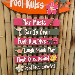 May include: A set of wooden signs with a tropical theme. The signs are hung on a bamboo wall and feature phrases like "Pool Rules", "Play Music", "Bar Is Open", "Push. Run. Dive", "Laugh. Splash. Play", "Float. Relax. Unwind", and "Good Times Expected".