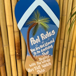 May include: A blue and white flip-flop shaped sign with the text "Pool Rules" and a palm tree graphic. The sign reads "You are not allowed to do anything that begins with the words "Hey Y'all Watch This".