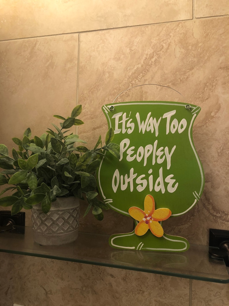 May include: Green wooden sign shaped like a margarita glass with the text "It's Way Too Peopley Outside". The sign has a yellow flower on the bottom.