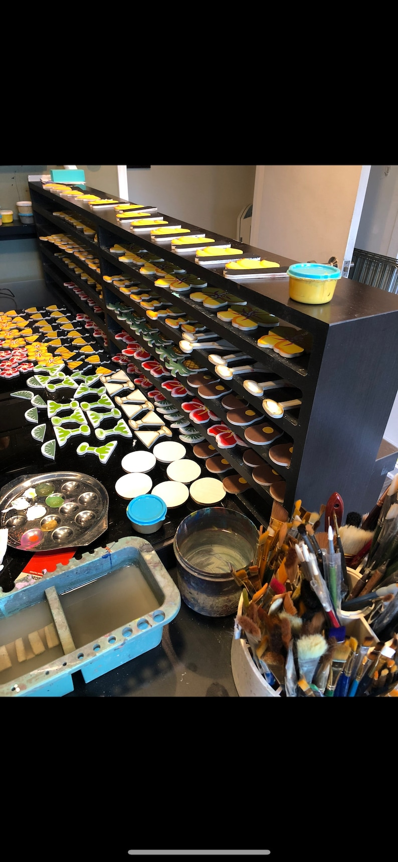 May include: A close-up of a work table with a variety of colorful ceramic tiles, paint, brushes, and other supplies. The tiles are arranged on shelves and are ready to be painted.