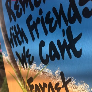 May include: A wooden sign with a blue, pink, and brown background. The sign has black painted text that reads "Remember with friends we can't forget..."