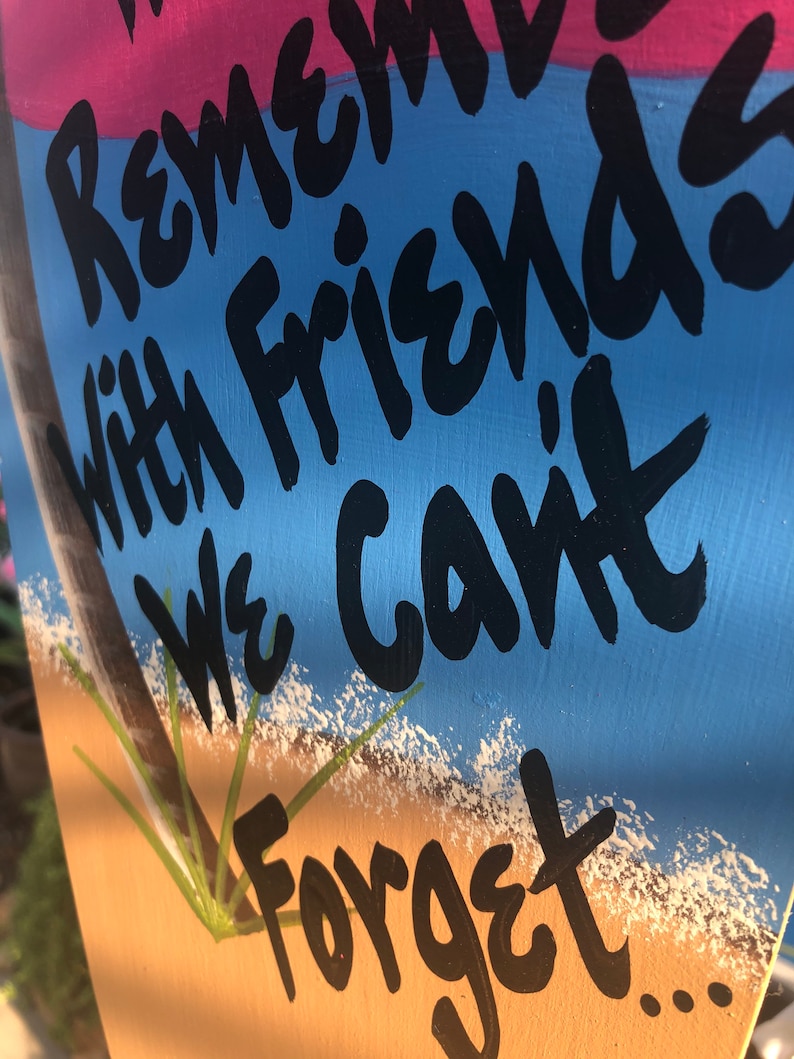 May include: A wooden sign with a blue, pink, and brown background. The sign has black painted text that reads "Remember with friends we can't forget..."