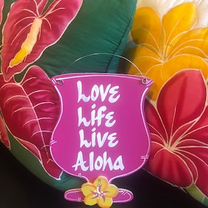 May include: Pink wooden sign shaped like a cocktail glass with the words "love life live Aloha" written in white. The sign is hanging from two small metal rings.