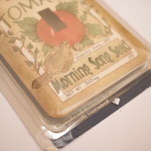May include: A vintage-style light switch cover with a brown background and a colorful illustration of a tomato plant, a bird, and the text "Morning Song Seed, Quality Seed, Net Wt. 300mg, 254,  Gauranteed, USA".