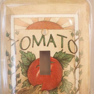 May include: A light switch cover with a vintage illustration of a tomato plant and the word "TOMATO" in a decorative font. The switch cover is made of clear plastic and has a white background.