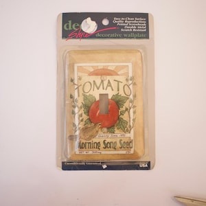 May include: A decorative light switch wall plate with a vintage-style illustration of a tomato plant and the text "TOMATO" and "Morning Song Seed".