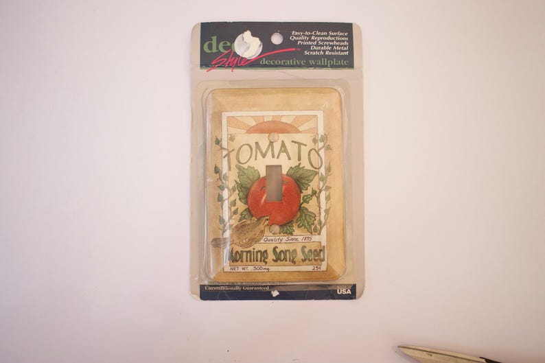 May include: A decorative light switch wall plate with a vintage-style illustration of a tomato plant and the text "TOMATO" and "Morning Song Seed".