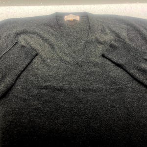 May include: A dark gray v-neck sweater made of a soft, knit fabric.