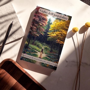 May include: A hardcover book titled Figlia dell'instabilità with a cover illustration of a person in a yellow dress walking on a forest path. The text at the bottom reads Il percorso di una bimba tra sfide e sogni. The book is rectangular.