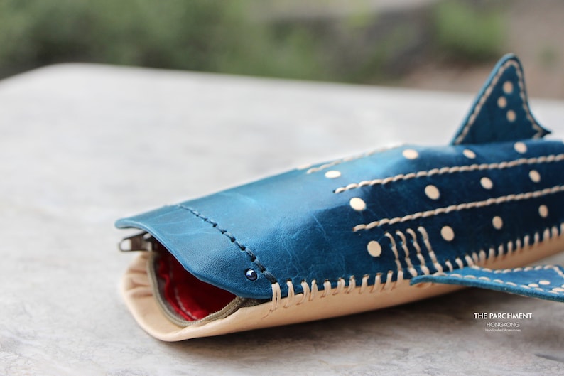 May include: A blue leather whale shark pencil case with white stitching and white polka dots. The case is open to reveal a red lining. The text "THE PARCHMENT HONGKONG" is visible in the bottom right corner.