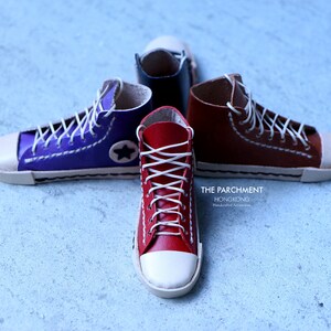 May include: Four miniature high-top sneakers in red, purple, brown, and black, with white laces and toe caps. The purple sneaker has a white star. The text "THE PARCHMENT HONGKONG" is visible.