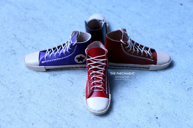May include: Four miniature high-top sneakers in red, purple, brown, and black, with white laces and toe caps. The purple sneaker has a white star. The text "THE PARCHMENT HONGKONG" is visible.