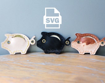 May include: Three leather piggy banks, one in beige, one in black, and one in brown, with a coin slot and a gold ring on the side. The piggy banks are on a wooden surface. The word "SVG" is written on a white file icon in the background.