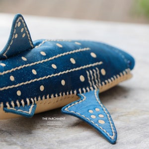 May include: A blue leather whale shark with white polka dots and white stitching. The shark is made of leather and has a stitched design.