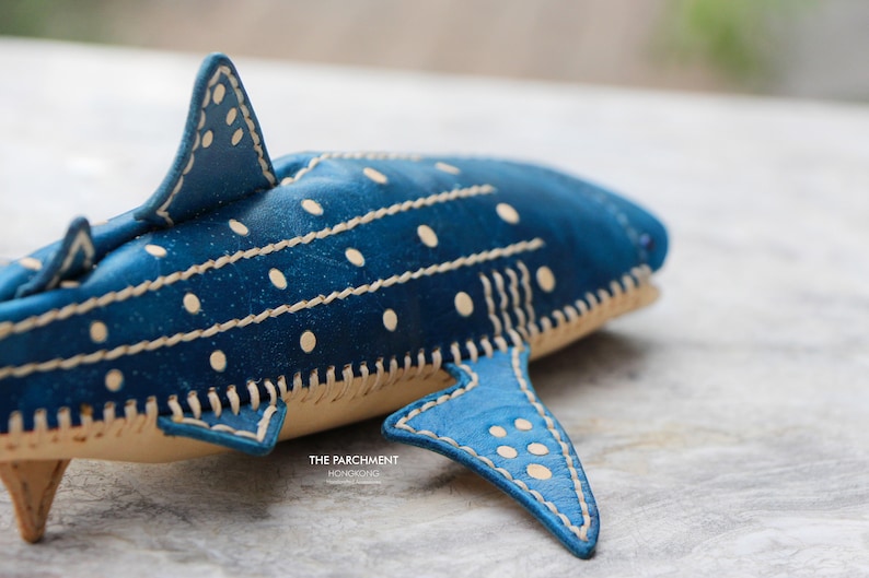 May include: A blue leather whale shark with white polka dots and white stitching. The shark is made of leather and has a stitched design.