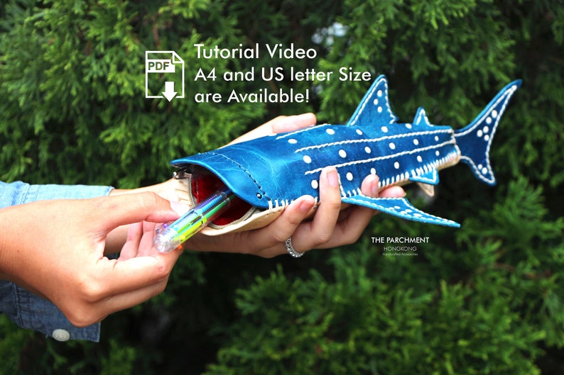 May include: A blue and white whale shark-shaped leather pencil case with white stitching. The case is open and a multi-coloured pen is being inserted. The text "Tutorial Video A4 and US letter size are Available!" is in the top left corner of the image.