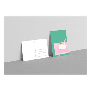May include: A postcard with a green background and a pink table with a white bowl of yellow food and a silver spoon on top. The other side of the postcard is blank with lines for writing.