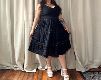 May include: A black tiered midi dress with a V-neckline and a studded design. The dress is made of a lightweight fabric and has a flowy silhouette.
