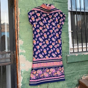 May include: A vintage sleeveless dress with a high neck and a floral print in shades of pink, orange, and blue on a navy background. The dress has a band of pink, orange, and blue trim around the bottom.