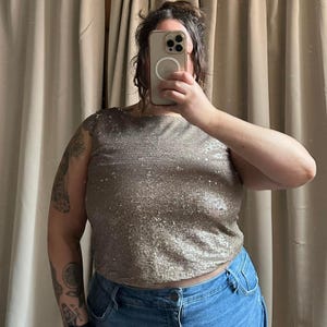 May include: A sleeveless, cropped top with a sparkly, silver and gold sequined fabric. The top has a scoop neck and a relaxed fit.