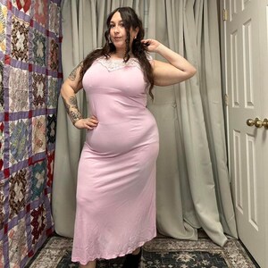 May include: A light pink slip dress with a lace trim neckline. The dress is sleeveless and has a flowing, midi-length skirt. The fabric appears to be a soft, lightweight material.