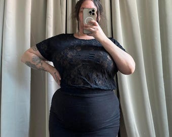 May include: A black lace top with short sleeves and a black mini skirt. The top is sheer and the skirt is fitted.