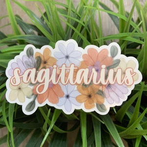 May include: A sticker featuring a floral design and the word "sagittarius" in a light orange colour.