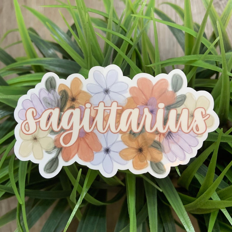 May include: A sticker featuring a floral design and the word "sagittarius" in a light orange colour.