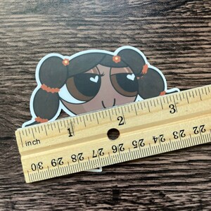 May include: A sticker of a cartoon character with brown hair, brown eyes, and a light brown complexion. The character has a white heart in each eye and is wearing a red flower in their hair. The sticker is about 1 inch tall.